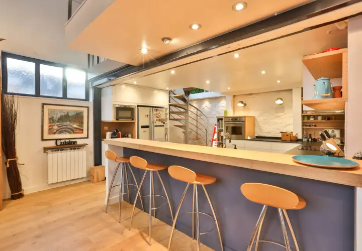Un bar fait maison original avec des tabourets orange vif, une cuisine moderne et un escalier en colimaçon.