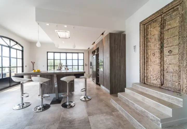 Cuisine moderne avec îlot central, tabourets chromés et une porte ancienne ornée. Un mélange audacieux de style Louis Philippe et contemporain.