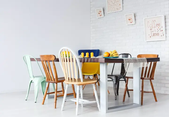 Un ensemble de chaises dépareillées entoure une table à manger. Des fruits et des bougies décorent la table.