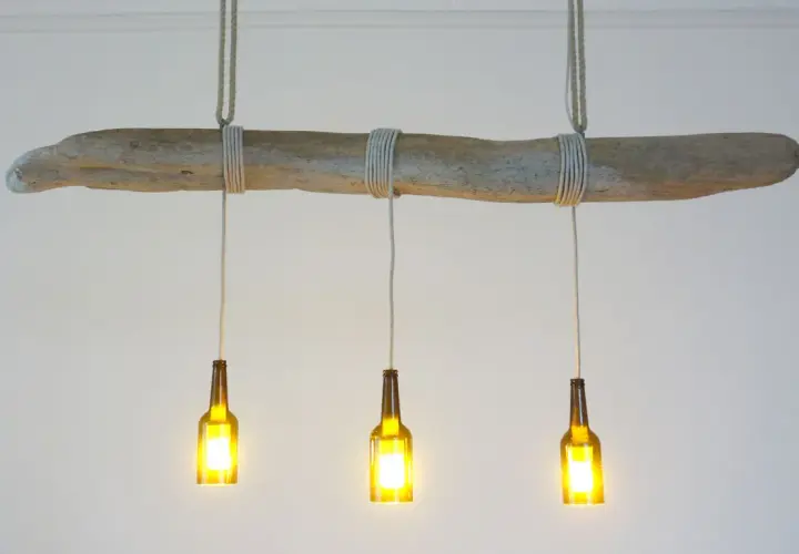 Lampe DIY originale : une branche flottée supporte trois bouteilles en verre ambré, transformées en luminaires.