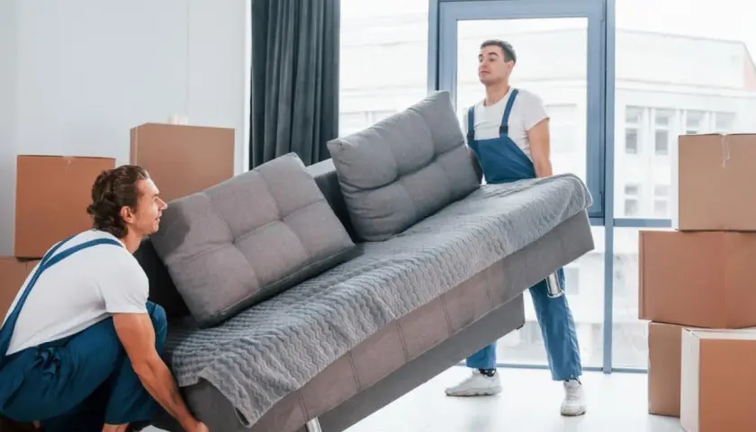 Deux déménageurs tentent de faire passer un canapé gris par une porte, mais la livraison du canapé ne passe pas la porte.