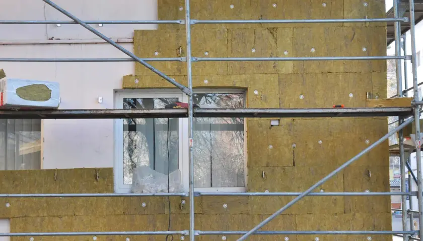 Échafaudage autour d'une maison en cours d'isolation avec de la laine de roche. Les panneaux isolants sont fixés sur le mur, prêts à isoler sa maison.