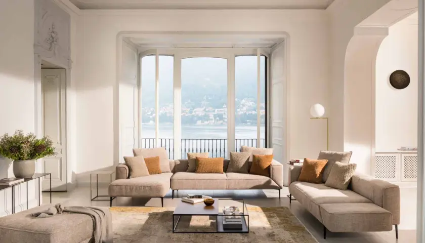 Un salon cocooning avec un canapé d'angle beige, des coussins douillets et une vue imprenable sur un lac.