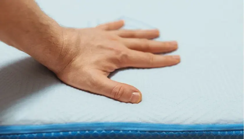 Main posée sur un matelas en mousse, testant son sens de confort et de soutien.