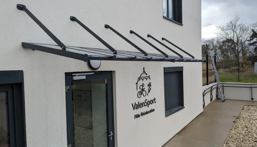 Une marquise moderne protège l'ouverture de la façade de cette maison, avec le logo ValenSport visible à côté de la porte.
