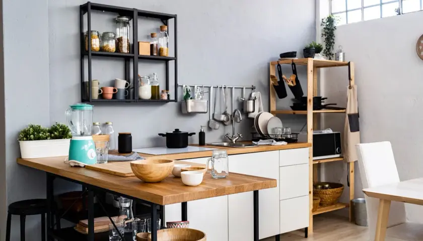 Une petite salle à manger moderne avec un îlot en bois, un mixeur turquoise et des étagères remplies d'ustensiles et d'épices.