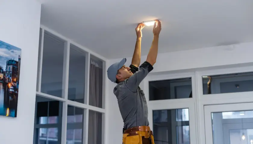 Un technicien installe un nouveau luminaire au plafond, un relamping définitif pour un éclairage moderne.