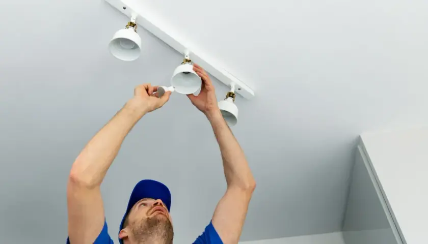 Un homme installe des spots LED sur un rail blanc. Le branchement en série ou parallèle de ces luminaires est en cours.