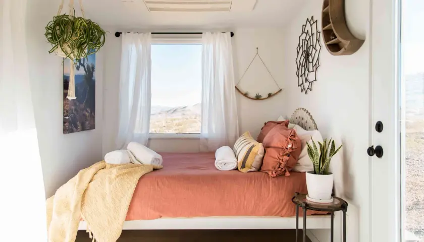 Une chambre d'amis cosy avec un lit orange, des coussins texturés, une couverture jaune et une vue désertique.