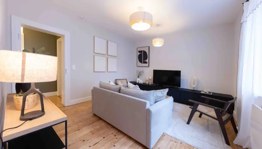 Salon moderne et lumineux, prêt à être habité. Le home staging met en valeur le canapé gris, le meuble TV noir et le parquet en bois.