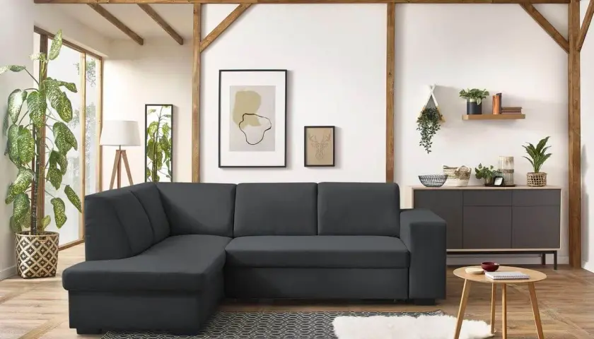 Un canapé d'angle gris foncé, parfait pour un salon feng shui, avec des poutres apparentes et des plantes vertes.