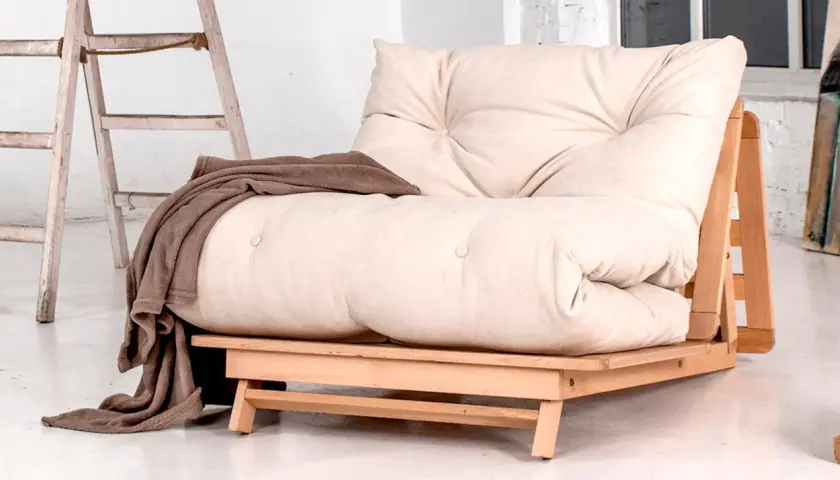 Un canapé futon beige avec une couverture marron drapée. Idéal pour savoir comment rendre un canapé plus confortable.