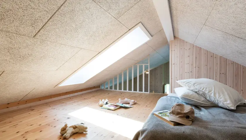 Chambre mansardée avec plafond texturé pour une excellente isolation phonique. Jouets sur le parquet, lit douillet.