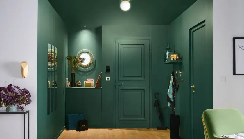 Une entrée chic et moderne avec des murs vert forêt, un miroir soleil, des sacs de shopping et une touche de plume de paon pour une deco entree élégante.