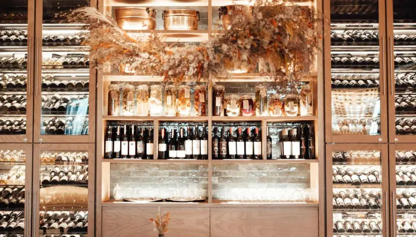 Éclairage cave à vin : étagères en bois remplies de bouteilles, bocaux et verres, le tout mis en valeur par une lumière douce et chaleureuse.