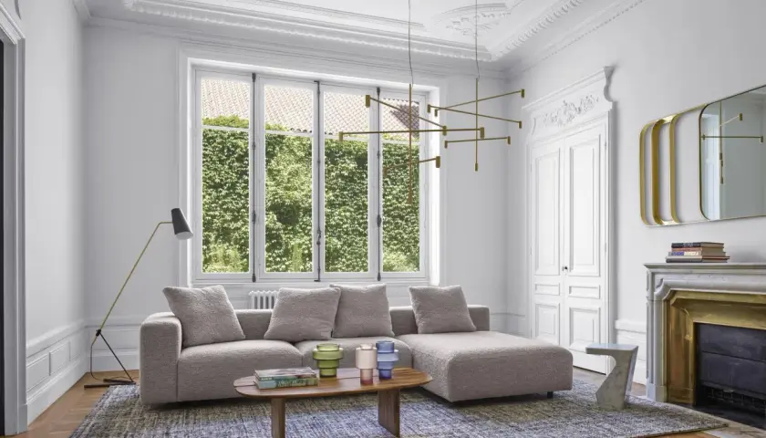 Salon moderne avec un grand canapé gris moelleux, une table basse en bois, un lustre doré et une cheminée ornée.