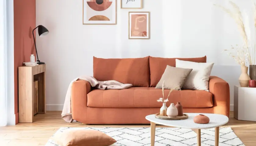 Canapé convertible orange, prêt à changer sommier. Déco bohème avec coussins, plaid et art mural.
