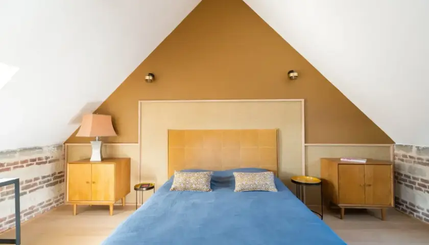 Chambre sous pente avec mur en **couleur ocre** et lit bleu. Meubles en bois vintage.