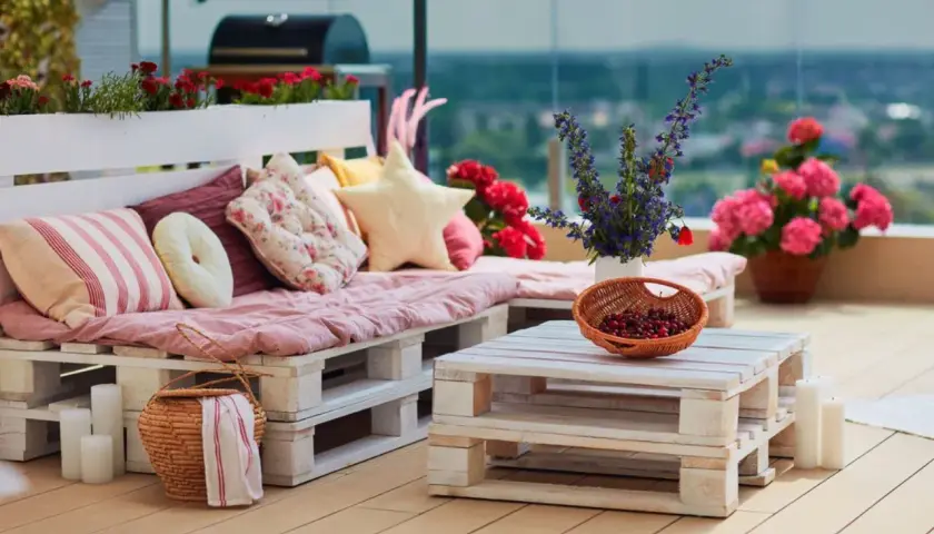 Un canapé en palette plan, confortable et coloré, orne cette terrasse avec des coussins douillets et des fleurs vives.