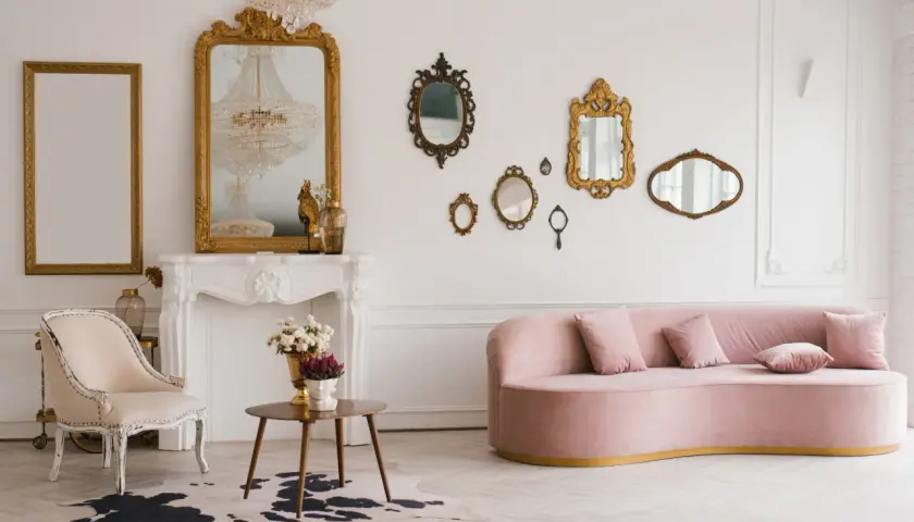 Un salon élégant avec un canapé rose, une chaise vintage, une cheminée ornée et une collection de miroirs dorés. Une déco salon vintage moderne réussie.