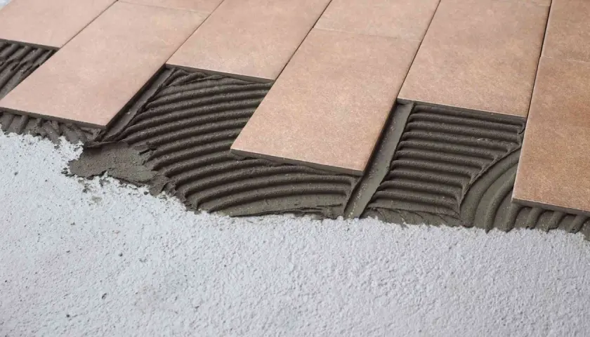 Pose de carrelage rectangulaire sur mortier frais. Les carreaux sont posés sur une couche de colle texturée, prêts à être ajustés.