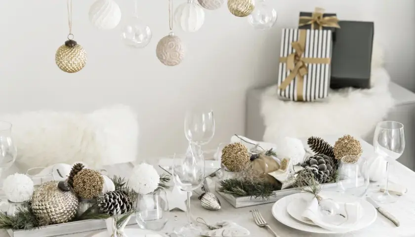 Une belle idée décoration table Noël : boules suspendues, centre de table naturel avec pommes de pin et ornements dorés, vaisselle élégante.