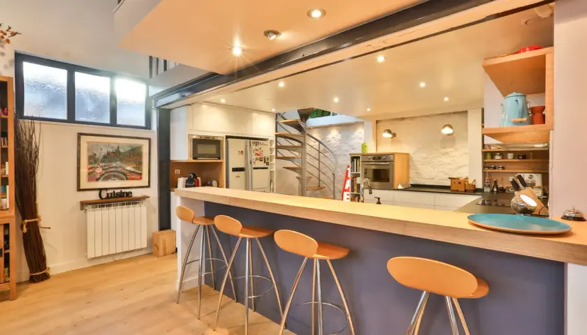 Un bar fait maison original avec des tabourets orange vif, une cuisine moderne et un escalier en colimaçon.