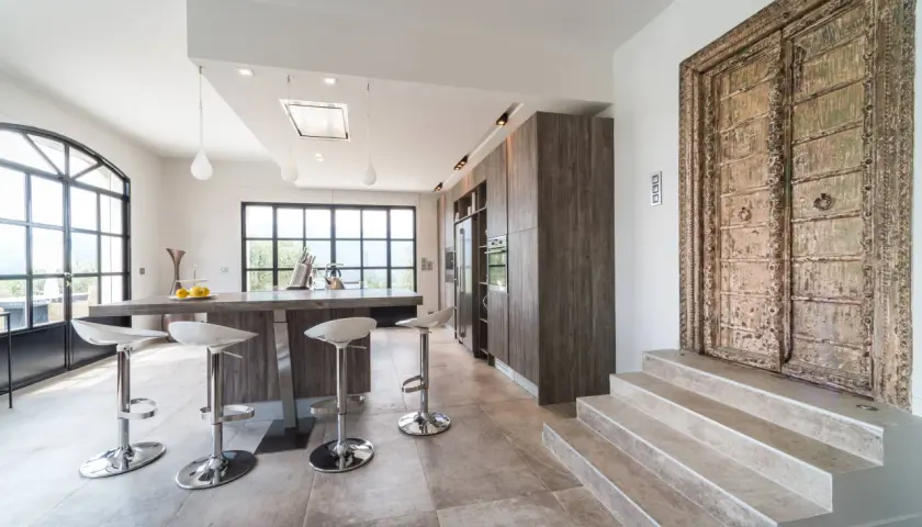 Cuisine moderne avec îlot central, tabourets chromés et une porte ancienne ornée. Un mélange audacieux de style Louis Philippe et contemporain.