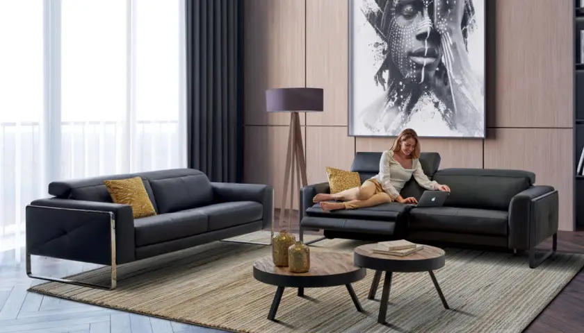 Salon moderne avec canapé noir, femme sur un fauteuil, tableau abstrait et tables basses.
