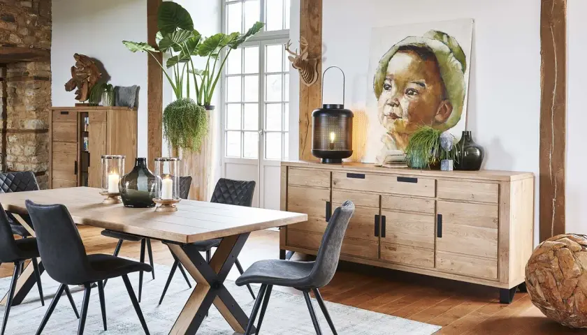 Une salle à manger avec une table en bois, des chaises grises et un buffet en chêne. Une belle idée déco salle à manger industrielle avec un tableau et des plantes.