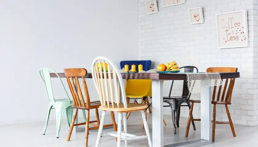 Un ensemble de chaises dépareillées entoure une table à manger. Des fruits et des bougies décorent la table.