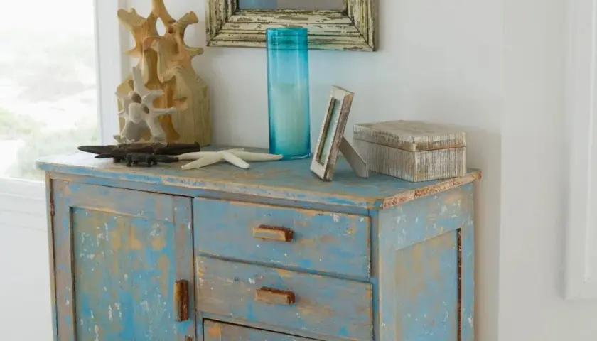 Meuble bleu délavé avec une patine bois effet vieilli, décoré d'objets marins et d'une boîte en bois.