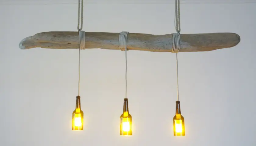 Lampe DIY originale : une branche flottée supporte trois bouteilles en verre ambré, transformées en luminaires.