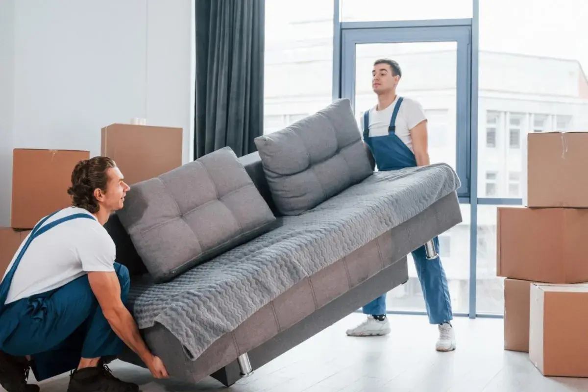 Deux déménageurs tentent de faire passer un canapé gris par une porte, mais la livraison du canapé ne passe pas la porte.