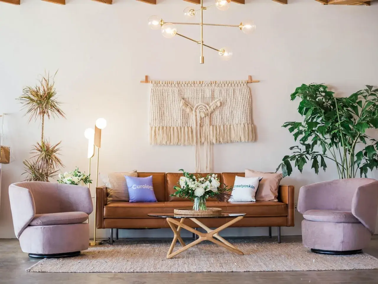 Salon moderne avec canapé en cuir marron, fauteuils roses poudrés et table basse en bois clair. Quelle couleur avec bois clair ? Le rose poudré et le marron s'harmonisent parfaitement.