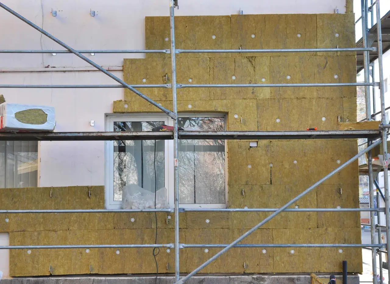 Échafaudage autour d'une maison en cours d'isolation avec de la laine de roche. Les panneaux isolants sont fixés sur le mur, prêts à isoler sa maison.