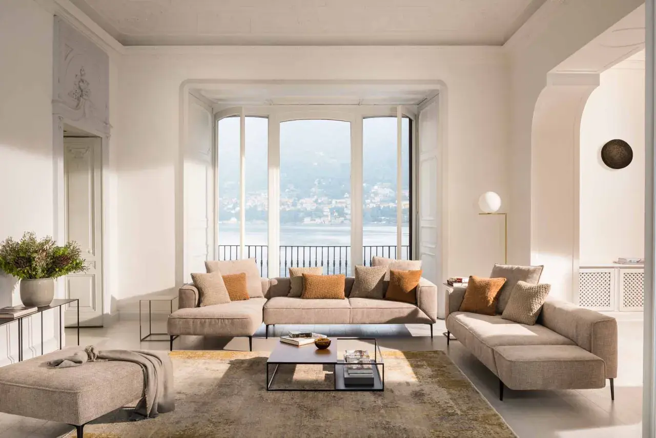 Un salon cocooning avec un canapé d'angle beige, des coussins douillets et une vue imprenable sur un lac.