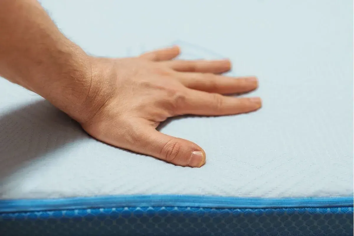 Main posée sur un matelas en mousse, testant son sens de confort et de soutien.