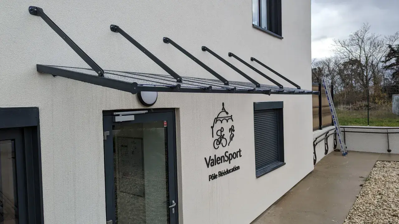 Une marquise moderne protège l'ouverture de la façade de cette maison, avec le logo ValenSport visible à côté de la porte.