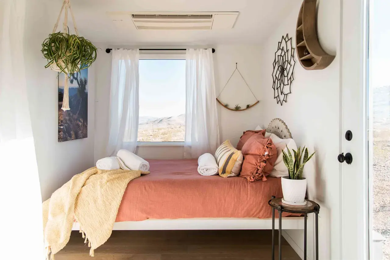 Une chambre d'amis cosy avec un lit orange, des coussins texturés, une couverture jaune et une vue désertique.