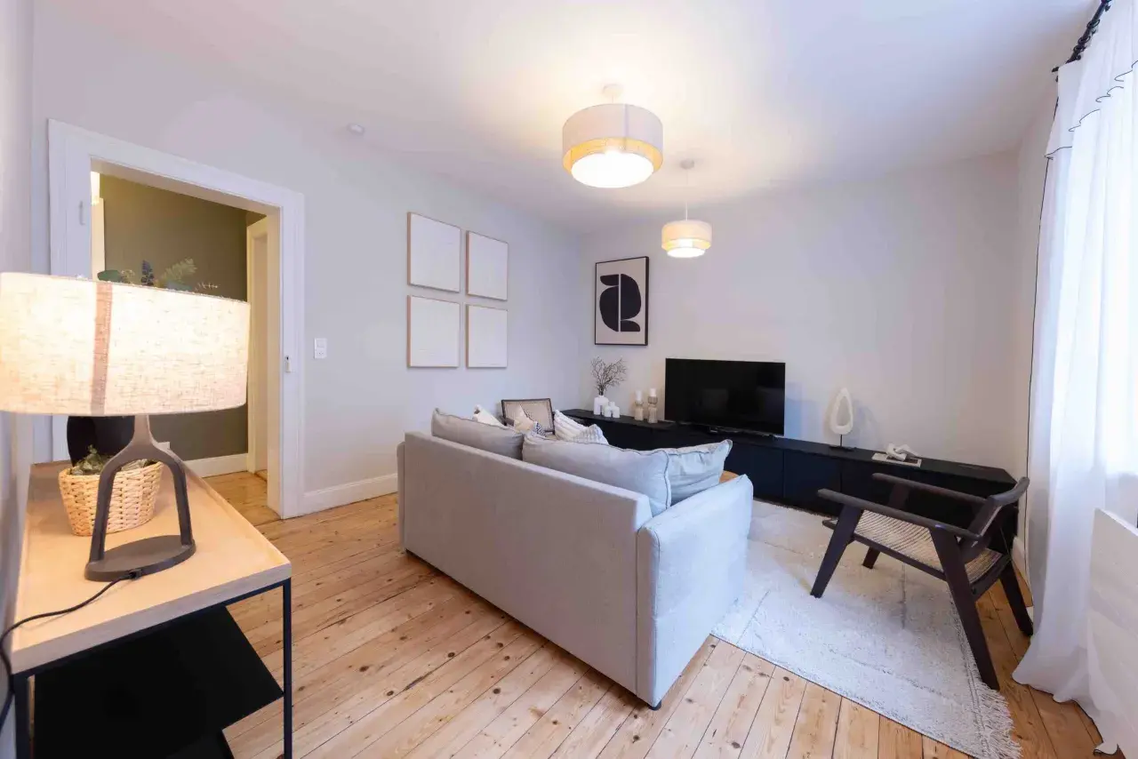 Salon moderne et lumineux, prêt à être habité. Le home staging met en valeur le canapé gris, le meuble TV noir et le parquet en bois.