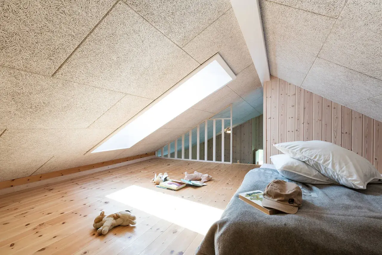 Chambre mansardée avec plafond texturé pour une excellente isolation phonique. Jouets sur le parquet, lit douillet.