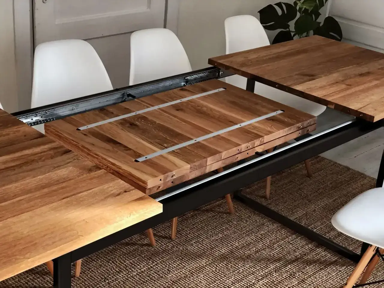 Détail du système de rallonge de table en bois, montrant les coulisses métalliques et les extensions empilées.