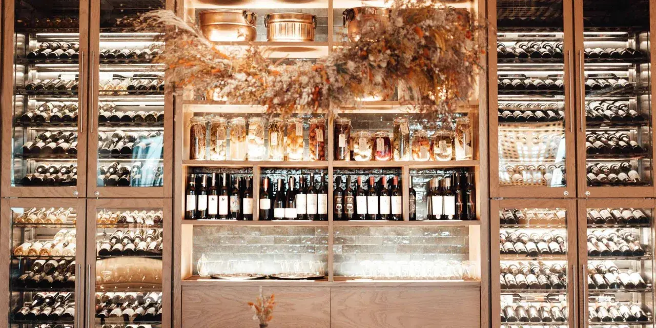 Éclairage cave à vin : étagères en bois remplies de bouteilles, bocaux et verres, le tout mis en valeur par une lumière douce et chaleureuse.