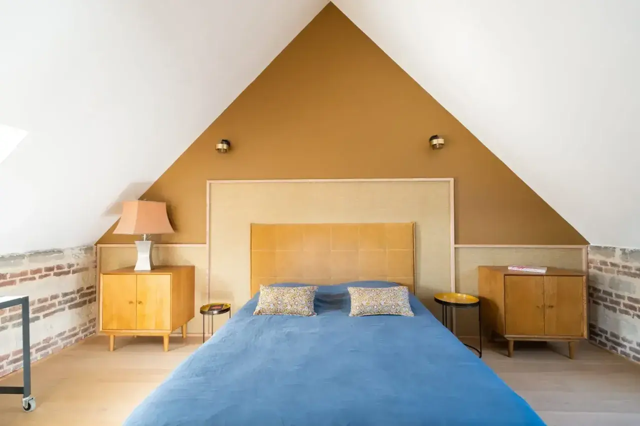 Chambre sous pente avec mur en **couleur ocre** et lit bleu. Meubles en bois vintage.