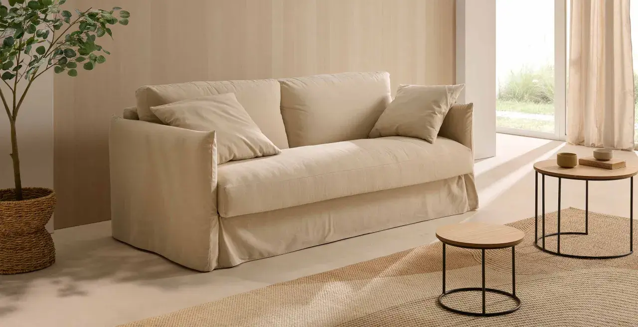 Un canapé beige confortable, des coussins douillets, une plante verte et des tables basses en bois. Quelle déco avec canapé beige pour un salon cosy et lumineux.