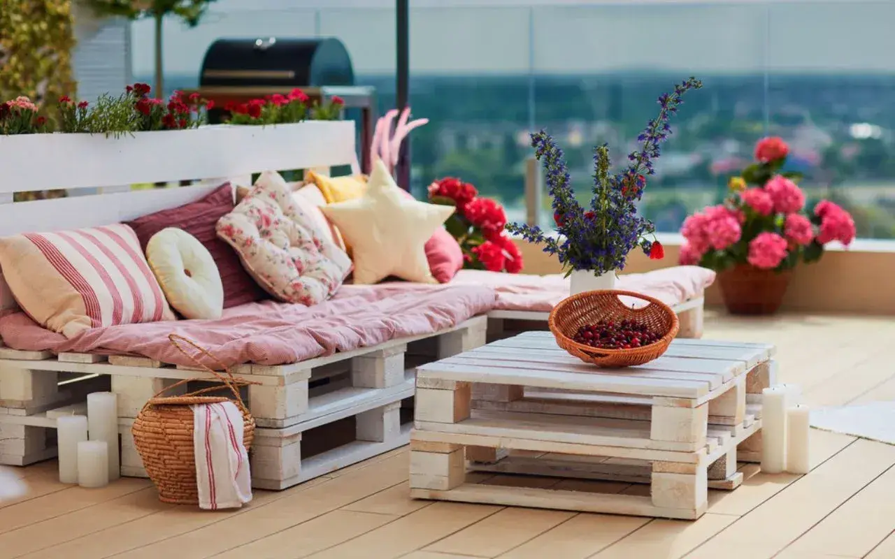 Un canapé en palette plan, confortable et coloré, orne cette terrasse avec des coussins douillets et des fleurs vives.