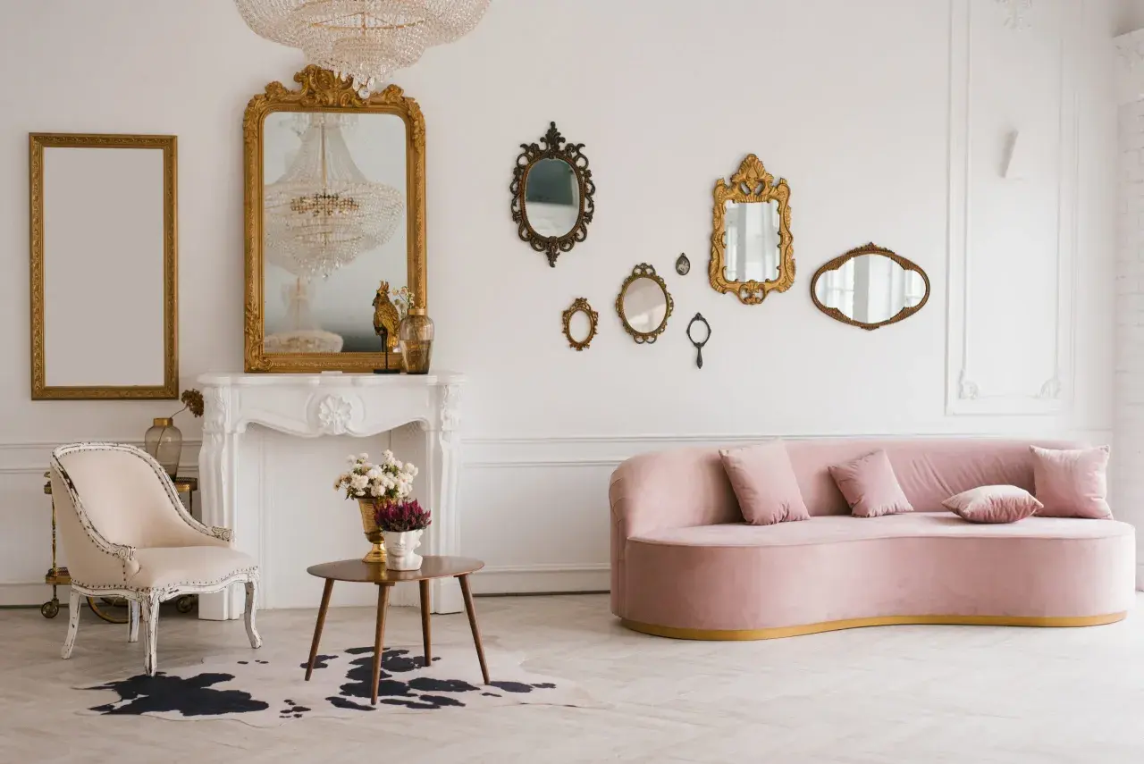 Un salon élégant avec un canapé rose, une chaise vintage, une cheminée ornée et une collection de miroirs dorés. Une déco salon vintage moderne réussie.