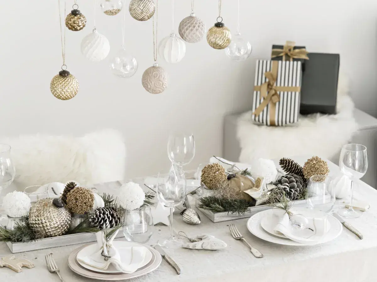 Une belle idée décoration table Noël : boules suspendues, centre de table naturel avec pommes de pin et ornements dorés, vaisselle élégante.