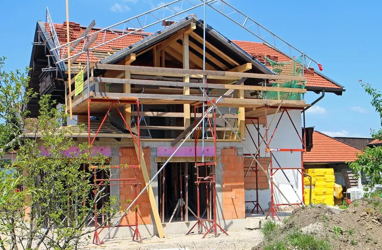 Une maison en pleine rénovation, avec échafaudages et matériaux de construction. Les propriétaires sont occupés à faire des travaux dans leur maison.